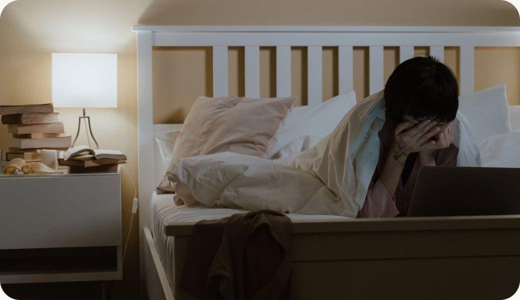 A woman in bed with her head in her hands beside a lamp